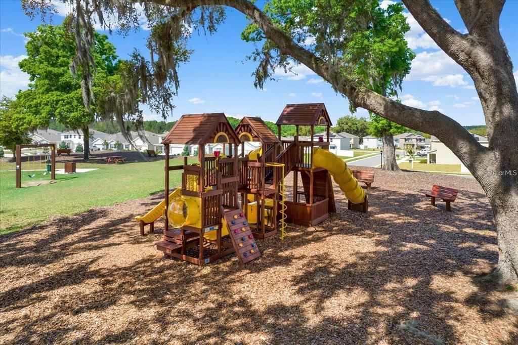 A wooden playground structure sits on a wood-chipped surface under large oak trees — 13688 WINEBERRY DRIVE, DADE CITY, FL
