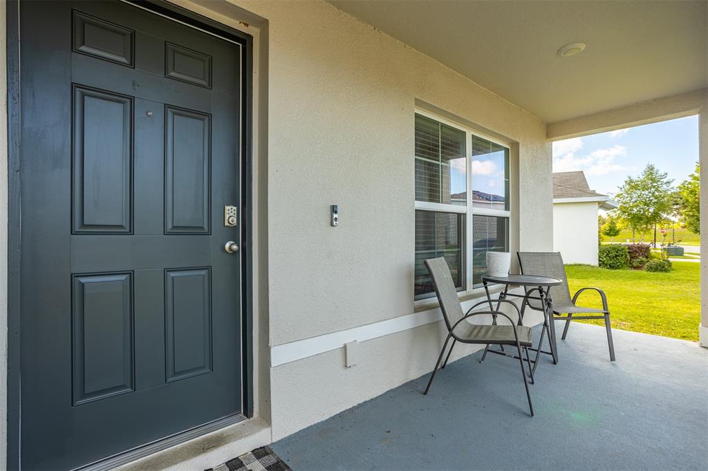 A covered front porch features a dark gray door, a window, and two patio chairs — 13688 WINEBERRY DRIVE, DADE CITY, FL