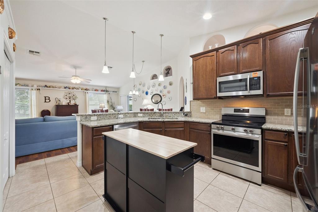 A kitchen with dark wood cabinets, granite countertops, stainless steel appliances, and a central island — 2243 WOLF RIDGE LANE, MOUNT DORA, FL
