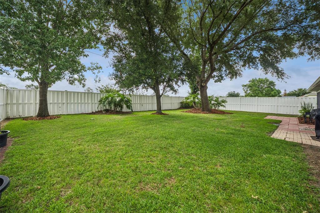 A grassy backyard features mature trees, a white vinyl privacy fence, and a brick patio — 2243 WOLF RIDGE LANE, MOUNT DORA, FL