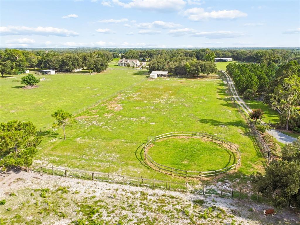 An aerial view shows a fenced pasture with a round pen and a distant house — 336 CORBETT ROAD, LITHIA, FL