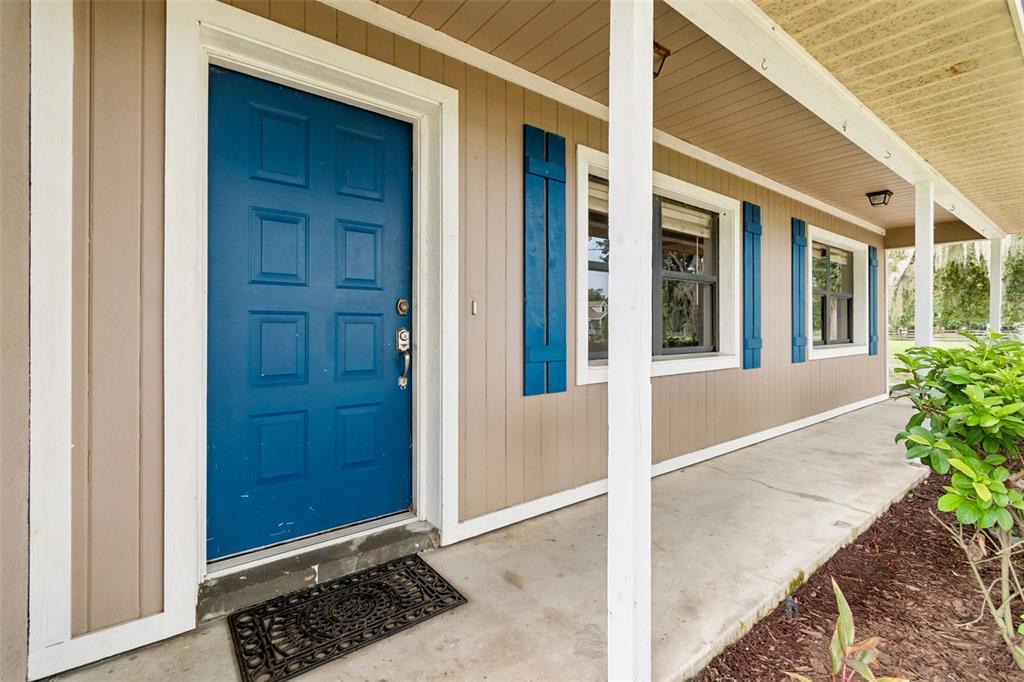 A blue front door with white trim sits on a covered porch with beige siding — 336 CORBETT ROAD, LITHIA, FL