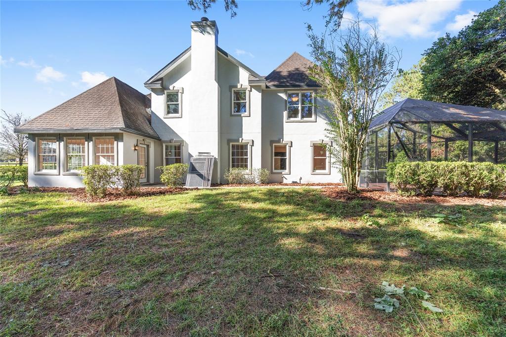 The rear exterior of a two-story stucco house features a chimney and a screened enclosure — 6581 S MAGNOLIA AVENUE, OCALA, FL