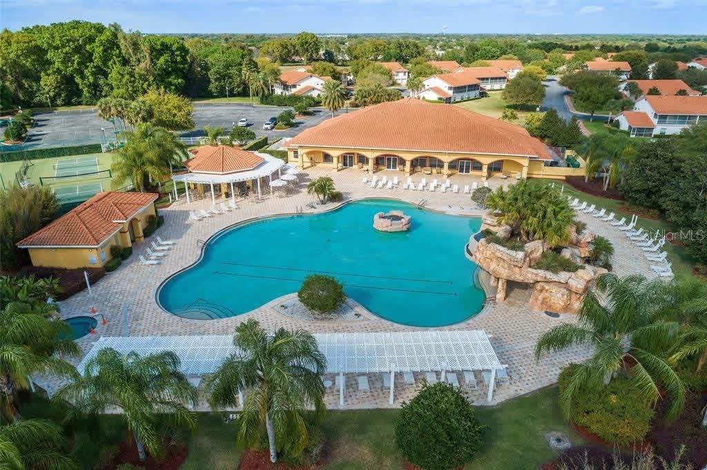 An aerial view of a community pool area with a clubhouse, tennis courts, and landscaping — 5011 BELTED KINGFISHER DRIVE, OXFORD, FL