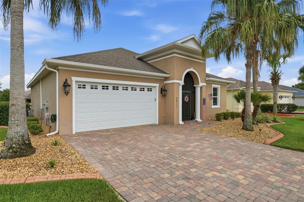 A tan single-story house with a two-car garage, arched entryway, and a paved driveway — 5011 BELTED KINGFISHER DRIVE, OXFORD, FL