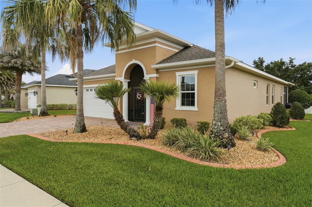 A tan single-story house with a paved driveway, palm trees, and a landscaped front yard — 5011 BELTED KINGFISHER DRIVE, OXFORD, FL