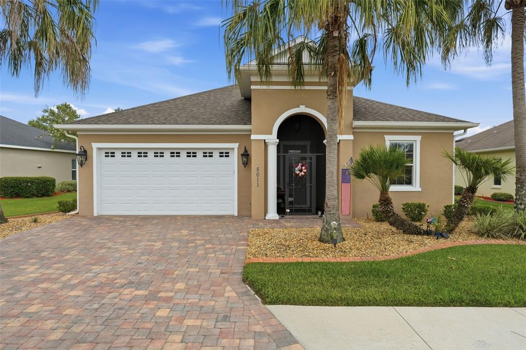 A single-story tan house with a two-car garage, arched entryway, and paved driveway — 5011 BELTED KINGFISHER DRIVE, OXFORD, FL