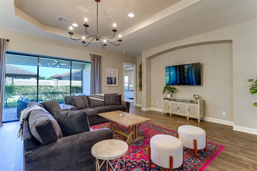 A living room features a dark sofa, a colorful rug, and a wall-mounted television — 5006 TIVOLI RUN, LAKEWOOD RANCH, FL