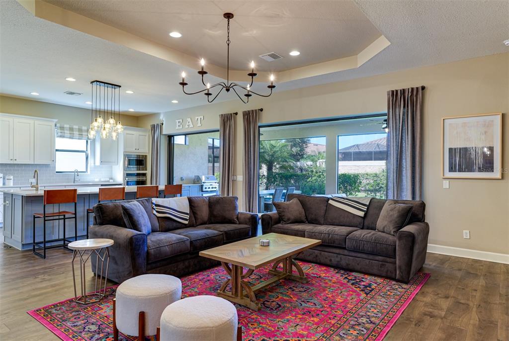 A living room with two dark sofas, a pink patterned rug, and an open kitchen — 5006 TIVOLI RUN, LAKEWOOD RANCH, FL