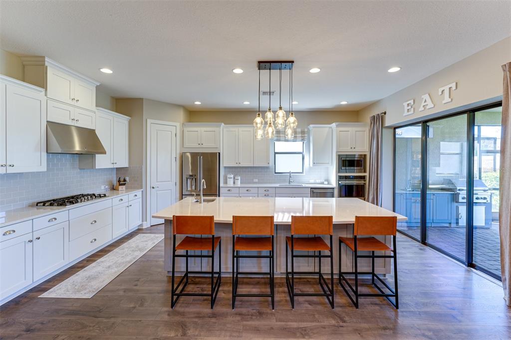 A modern kitchen features white cabinetry, a large central island with four stools, and stainless appliances — 5006 TIVOLI RUN, LAKEWOOD RANCH, FL