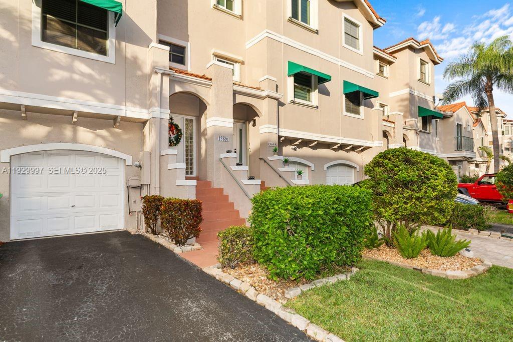 A multi-story townhouse exterior features a white garage door, stairs, and green window awnings — 12691 NW 14th Pl, Sunrise FL 33323, SUNRISE, FL