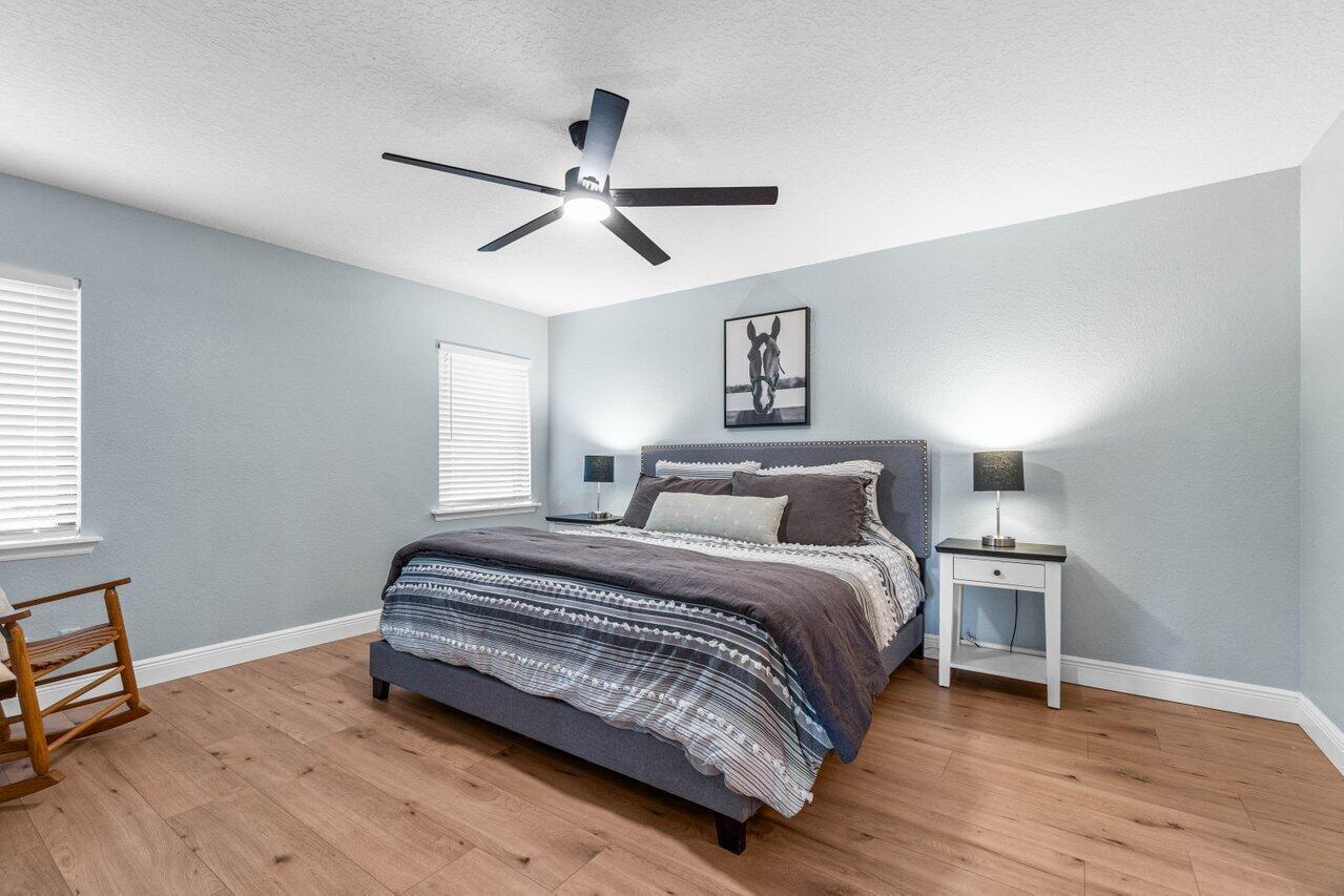 A bedroom features light blue walls, wood-look flooring, a ceiling fan, and a gray bed — 3303 Custer Avenue, Lake Worth FL 33467, LAKE WORTH, FL