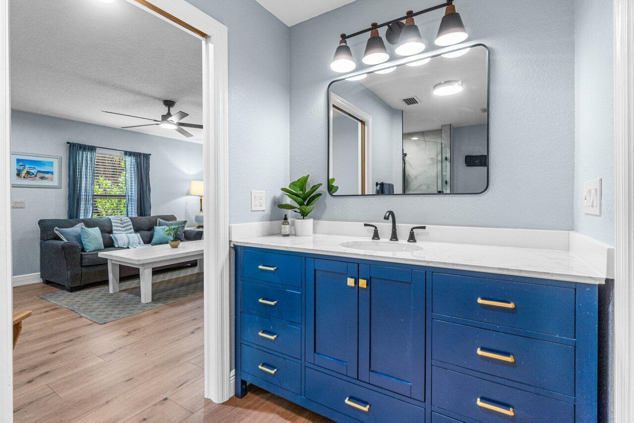 A bathroom features a blue vanity with gold hardware, a white countertop, and a mirror — 3303 Custer Avenue, Lake Worth FL 33467, LAKE WORTH, FL