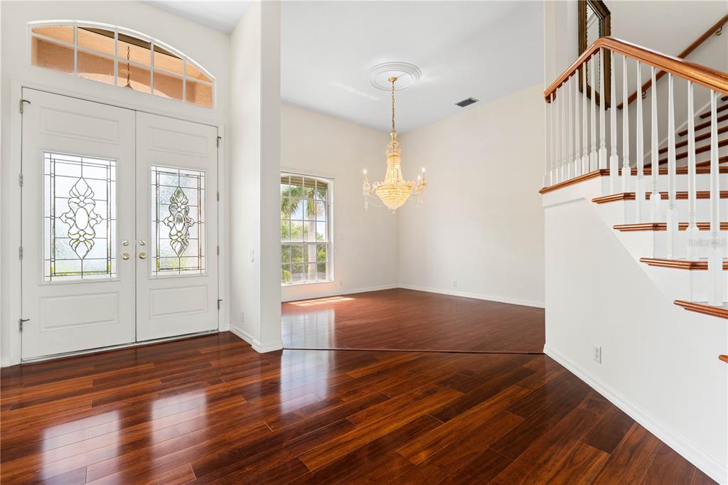 An entryway with dark wood floors, a crystal chandelier, and a staircase with white railings — 250 GEORGE ROAD, PORT CHARLOTTE, FL