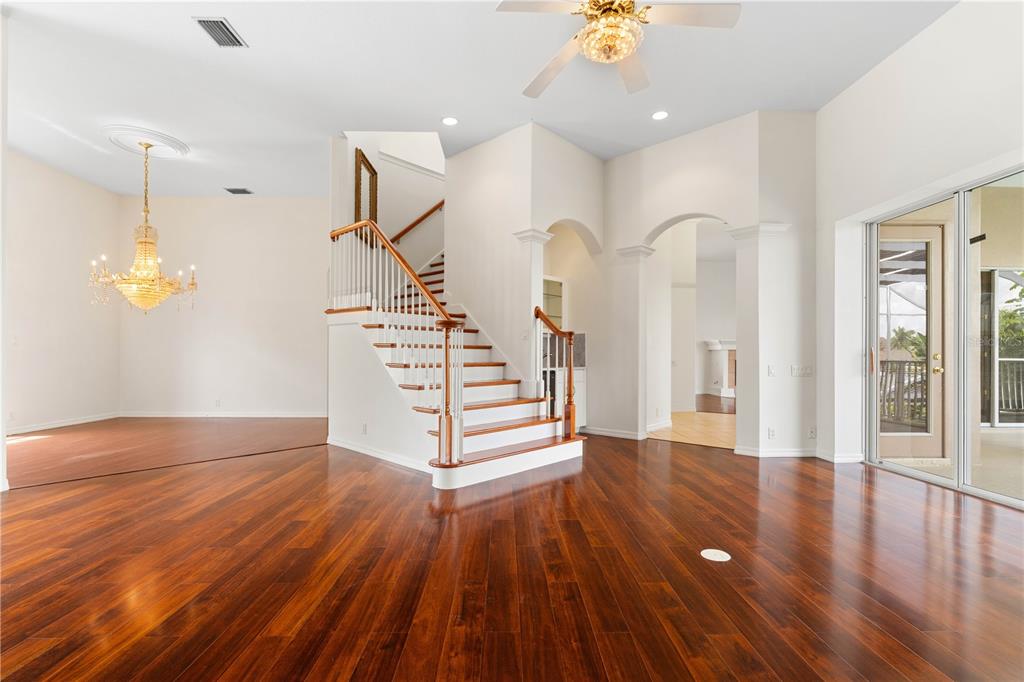 A spacious room with dark wood flooring, a central staircase, and a crystal chandelier — 250 GEORGE ROAD, PORT CHARLOTTE, FL