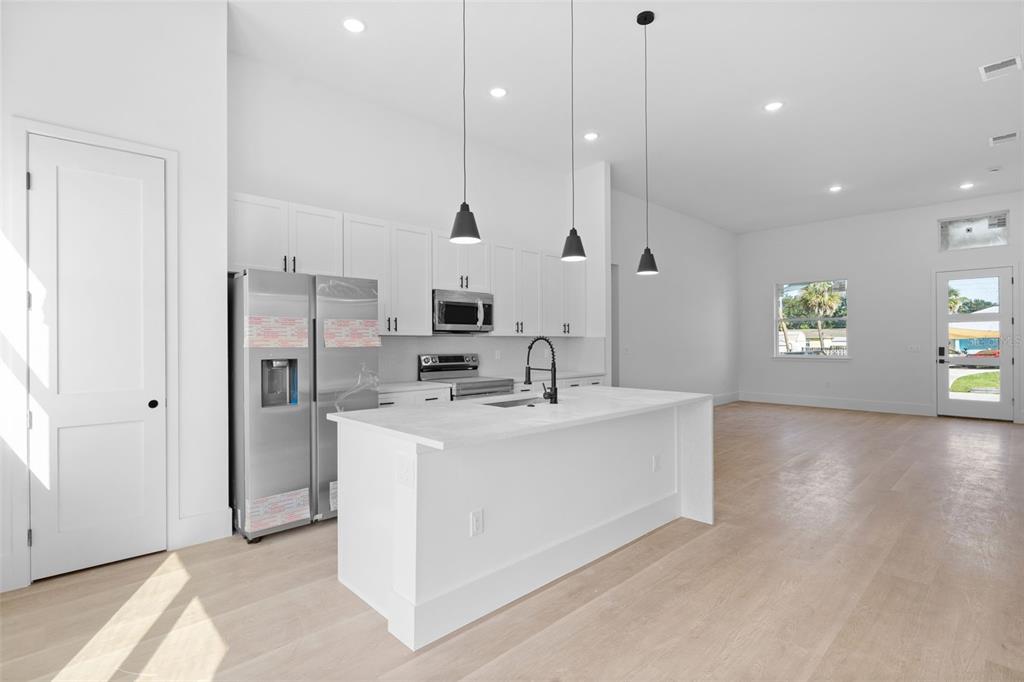 A modern kitchen features white cabinetry, stainless steel appliances, a center island, and light flooring — 543 CHAMBER STREET NW, PORT CHARLOTTE, FL