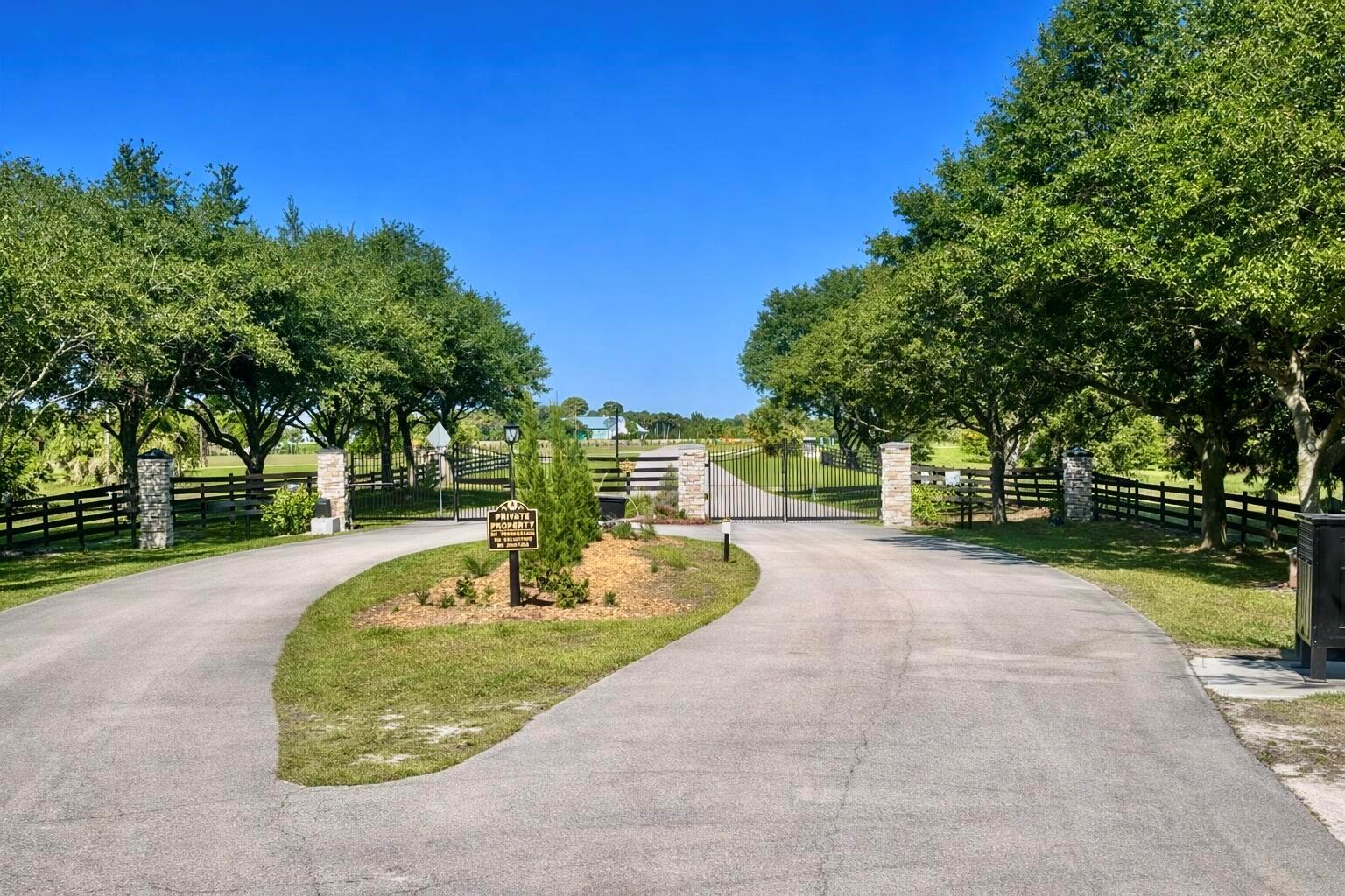 A paved driveway leads to a gated entrance flanked by stone pillars and green trees — 2452 SE 130th Way, Okeechobee FL 34974, OKEECHOBEE, FL