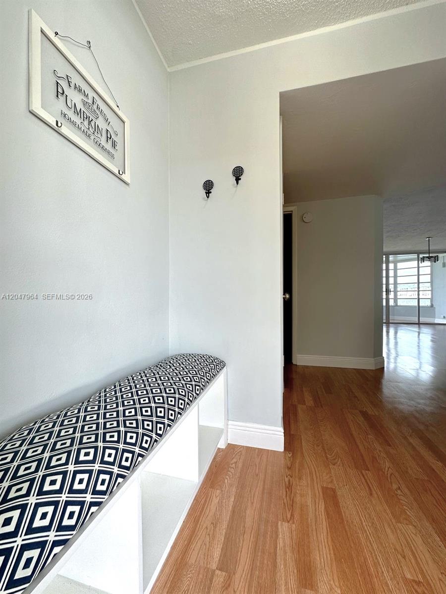 An entryway features a white storage bench with a patterned cushion and wall-mounted hooks — 1300 NE 191st St # A112, Miami FL 33179, MIAMI, FL