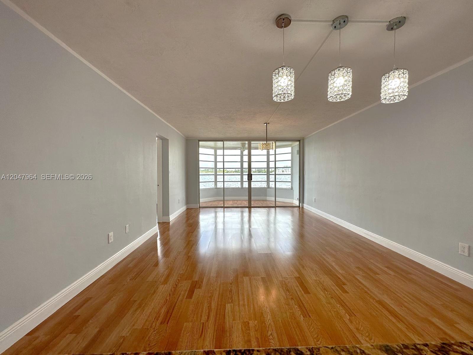 An empty room features light gray walls, hardwood floors, and a balcony with water views — 1300 NE 191st St # A112, Miami FL 33179, MIAMI, FL