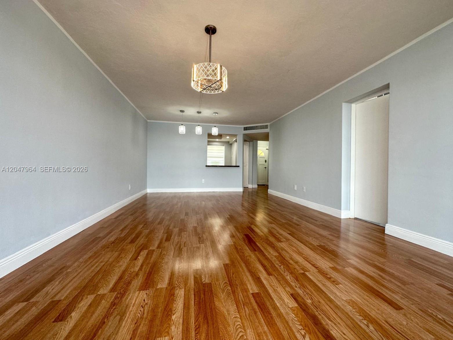 An empty room features light blue walls, hardwood flooring, and several hanging light fixtures — 1300 NE 191st St # A112, Miami FL 33179, MIAMI, FL