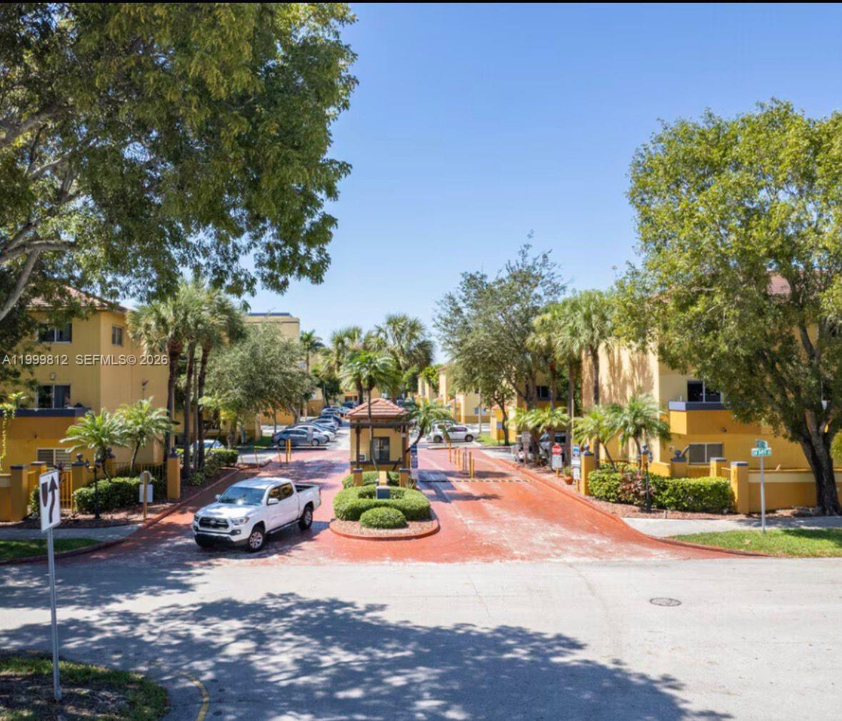 A gated entrance with a guardhouse leads into a residential complex with yellow apartment buildings — 8270 SW 149th Ct # 209, Miami FL 33193, MIAMI, FL