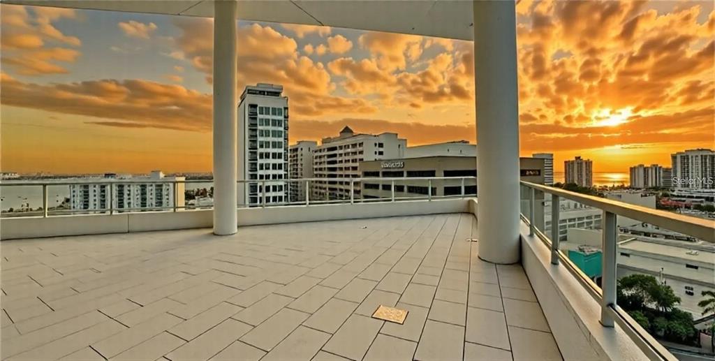 A spacious balcony with tiled flooring and a metal railing overlooks a city skyline at sunset — 111 S PINEAPPLE AVENUE UNIT 1210, SARASOTA, FL