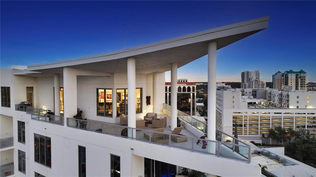 A high-angle view of a modern penthouse terrace with white pillars and outdoor furniture — 111 S PINEAPPLE AVENUE UNIT 1210, SARASOTA, FL
