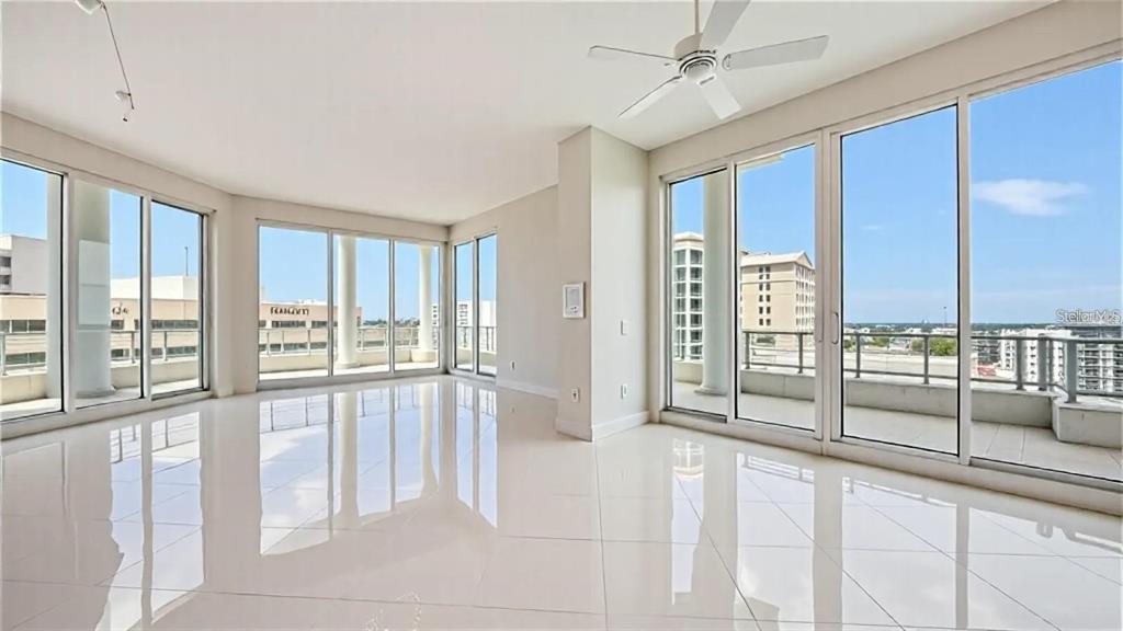 A bright, empty room features white tile floors, a ceiling fan, and floor-to-ceiling glass doors — 111 S PINEAPPLE AVENUE UNIT 1210, SARASOTA, FL