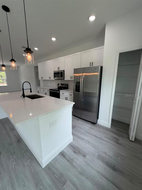 A modern kitchen features white cabinets, stainless steel appliances, a quartz island, and gray flooring — 5978 SW 154TH LANE ROAD, OCALA, FL