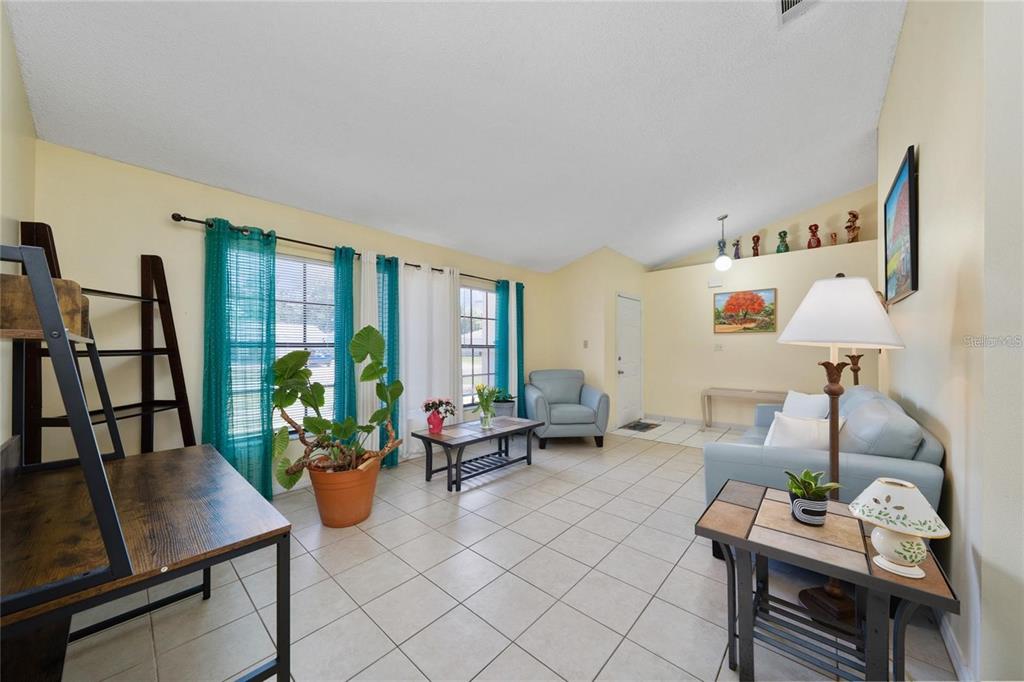 A living room with light-colored tile floors, yellow walls, and a vaulted ceiling — 307 COLONY COURT, KISSIMMEE, FL