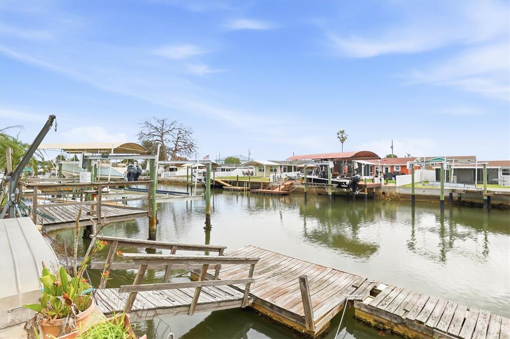 A wooden dock features a boat lift and metal chairs overlooking a canal with boats — 13538 LESLIE DRIVE, HUDSON, FL