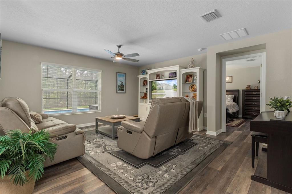 A living room features a beige sofa, a recliner, a media center, and wood-look flooring — 17528 GARSALASO CIRCLE, BROOKSVILLE, FL