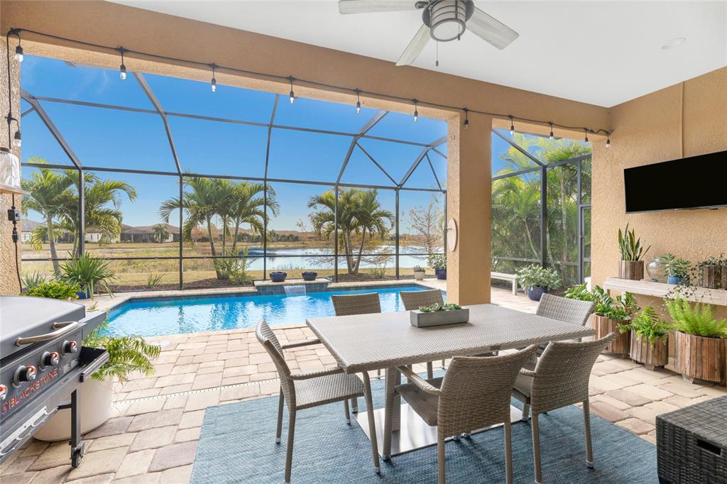 A covered patio features a dining set, a pool, and a view of a lake — 26853 WEISKOPF DRIVE, ENGLEWOOD, FL
