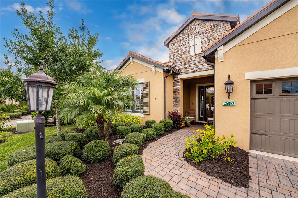 A stone-accented house exterior features a brick walkway, manicured shrubs, and a palm tree — 26853 WEISKOPF DRIVE, ENGLEWOOD, FL