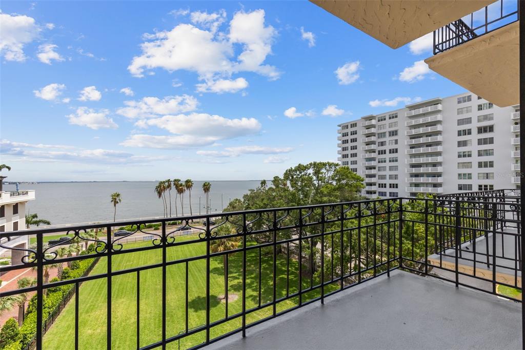 A balcony with a black metal railing overlooks a grassy lawn, palm trees, and the ocean — 2109 BAYSHORE BOULEVARD UNIT 503, TAMPA, FL