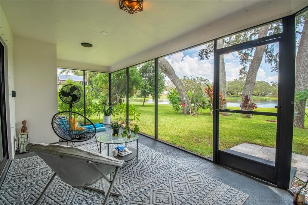 A screened-in porch with a patterned rug, patio furniture, and a view of a lake — 2906 WINDRIDGE DRIVE, HOLIDAY, FL