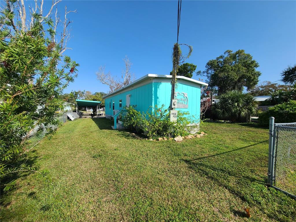 A bright turquoise mobile home sits on a grassy lot with a chain-link fence — 5418 CIRCLE DRIVE, WEEKI WACHEE, FL