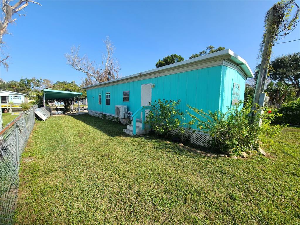 A bright turquoise mobile home sits on a grassy lot with a metal carport nearby — 5418 CIRCLE DRIVE, WEEKI WACHEE, FL