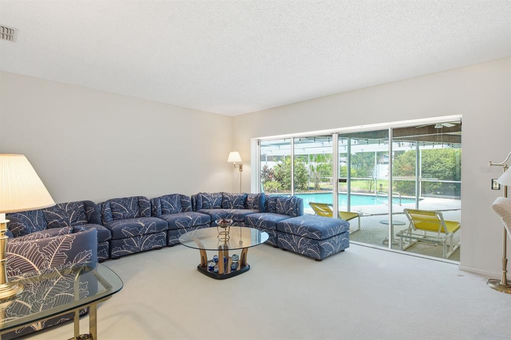 A living room features a large blue patterned sectional sofa, glass coffee tables, and pool views — 2768 NORTHRIDGE DRIVE E, CLEARWATER, FL