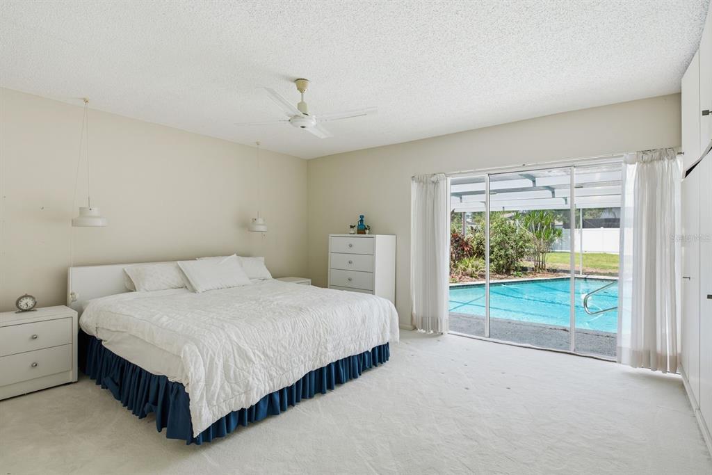 A bedroom with white carpet, a bed, a dresser, and sliding doors opening to a pool — 2768 NORTHRIDGE DRIVE E, CLEARWATER, FL