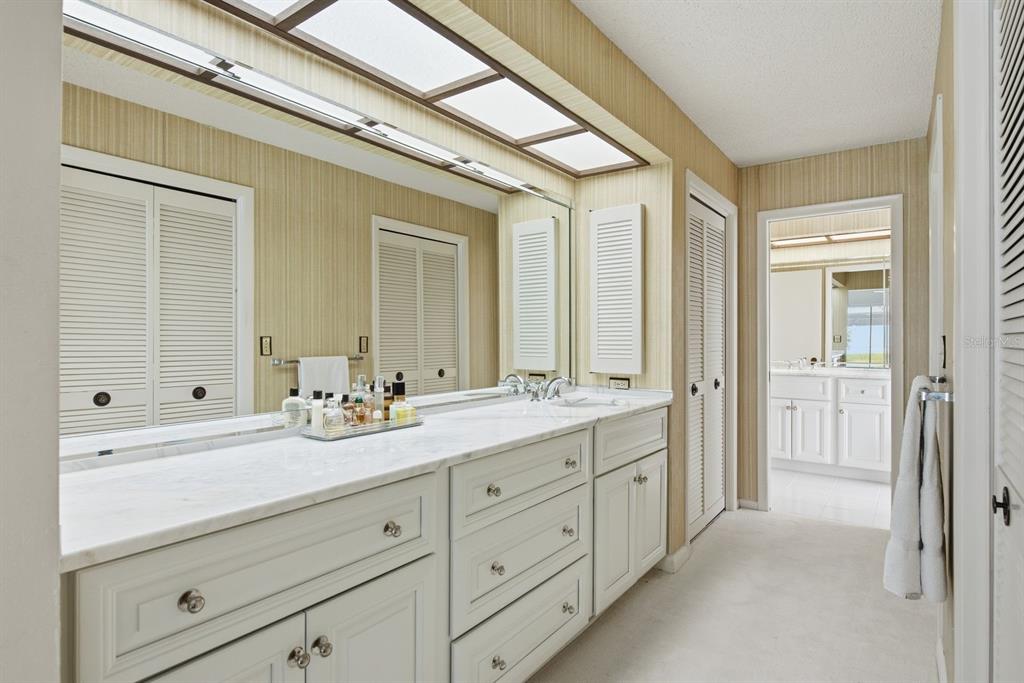 A bathroom features a long white vanity with a marble countertop, large mirror, and wallpaper — 2768 NORTHRIDGE DRIVE E, CLEARWATER, FL
