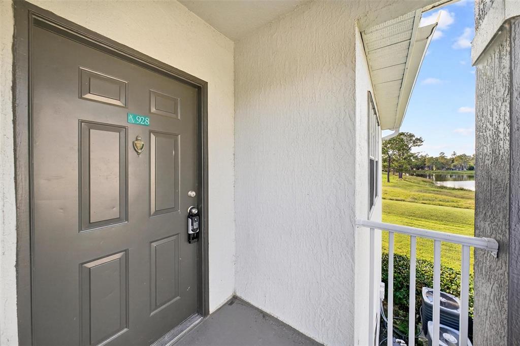 A gray front door with a digital lock is located on a covered outdoor balcony — 13917 FAIRWAY ISLAND DRIVE UNIT 928, ORLANDO, FL