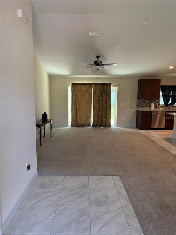 A living room with carpeted flooring transitions into a kitchen with dark wood cabinets — 3770 SE 137TH LANE, SUMMERFIELD, FL
