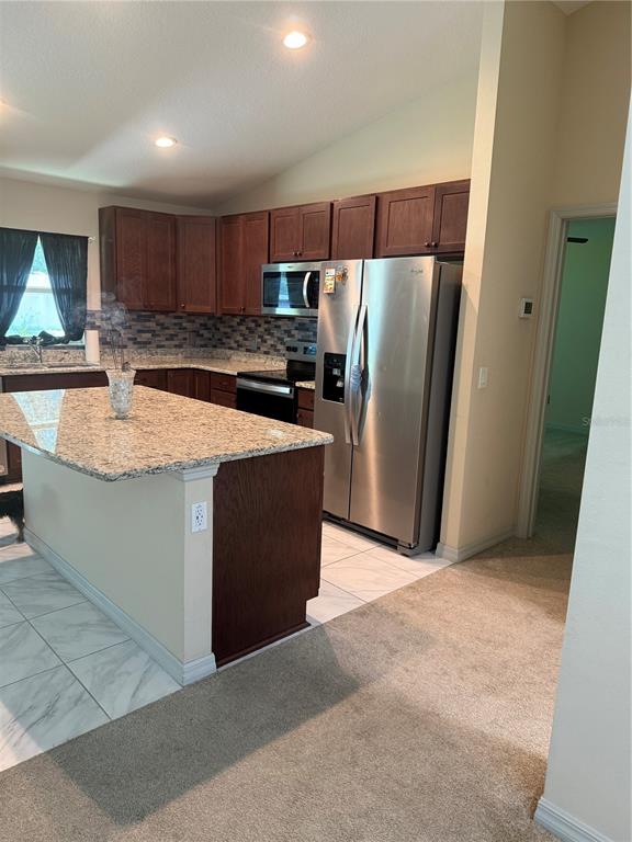 A kitchen features dark wood cabinets, granite countertops, a center island, and stainless steel appliances — 3770 SE 137TH LANE, SUMMERFIELD, FL