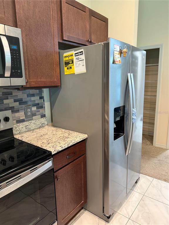 A kitchen features stainless steel appliances, dark wood cabinets, granite countertops, and a tiled backsplash — 3770 SE 137TH LANE, SUMMERFIELD, FL