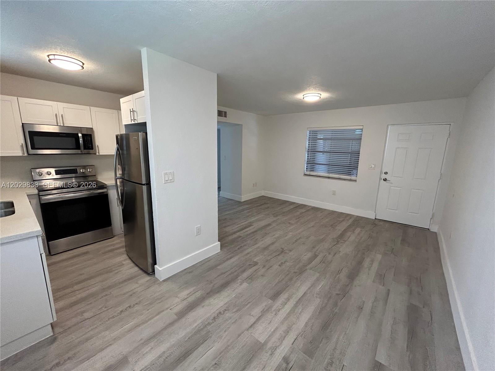 A kitchen with stainless steel appliances opens into a living area with wood-look flooring — 5960 W 25th Ct # 102, Hialeah FL 33016, HIALEAH, FL