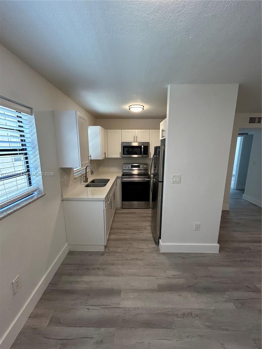 A galley kitchen features white cabinets, stainless steel appliances, and light-colored wood-look flooring — 5960 W 25th Ct # 102, Hialeah FL 33016, HIALEAH, FL