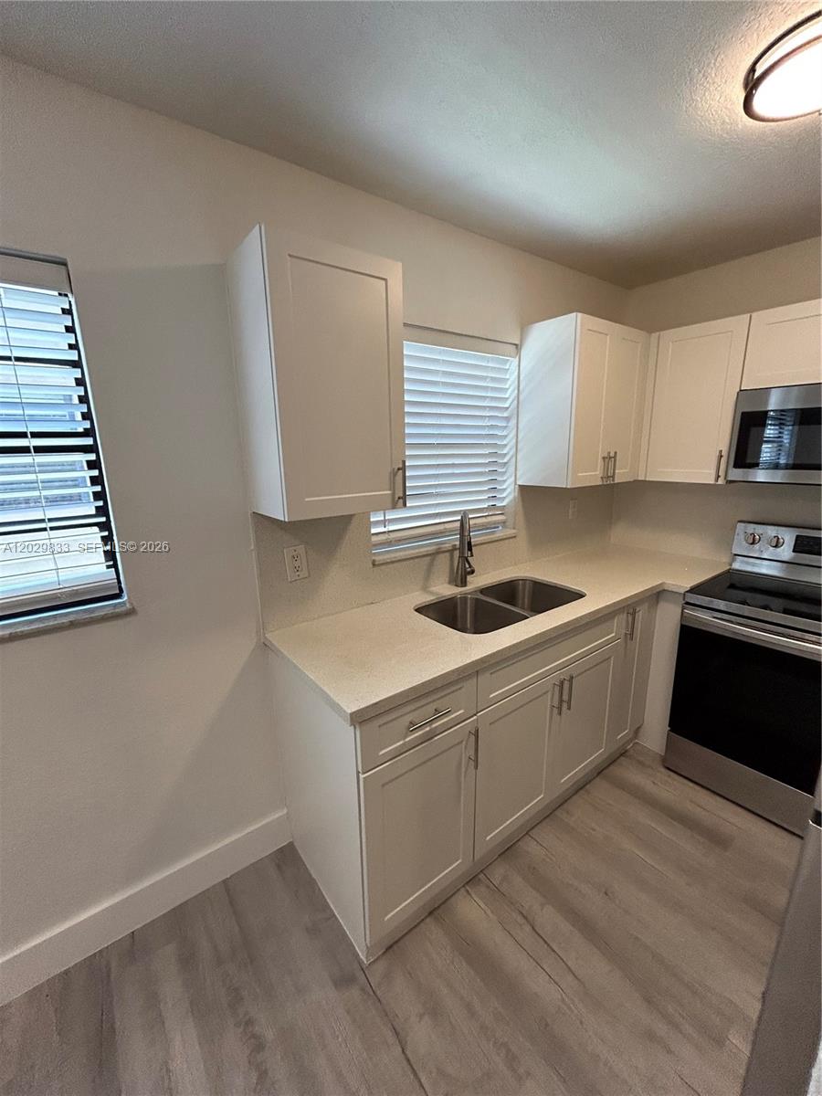 A kitchen features white cabinets, light countertops, stainless steel appliances, and wood-look flooring — 5960 W 25th Ct # 102, Hialeah FL 33016, HIALEAH, FL