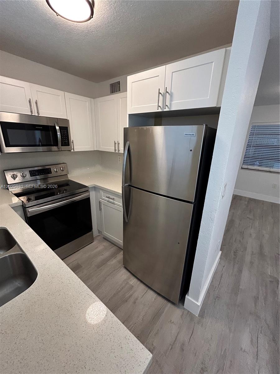 A modern kitchen features white cabinets, stainless steel appliances, and light-colored quartz countertops — 5960 W 25th Ct # 102, Hialeah FL 33016, HIALEAH, FL