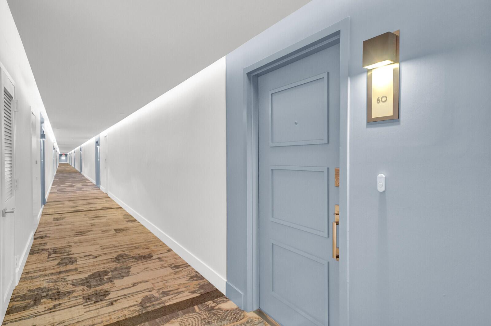 A long hotel hallway features light blue doors, patterned carpeting, and modern wall-mounted light fixtures — 1000 S Ocean Boulevard # o, Pompano Beach FL 33062, POMPANO BEACH, FL